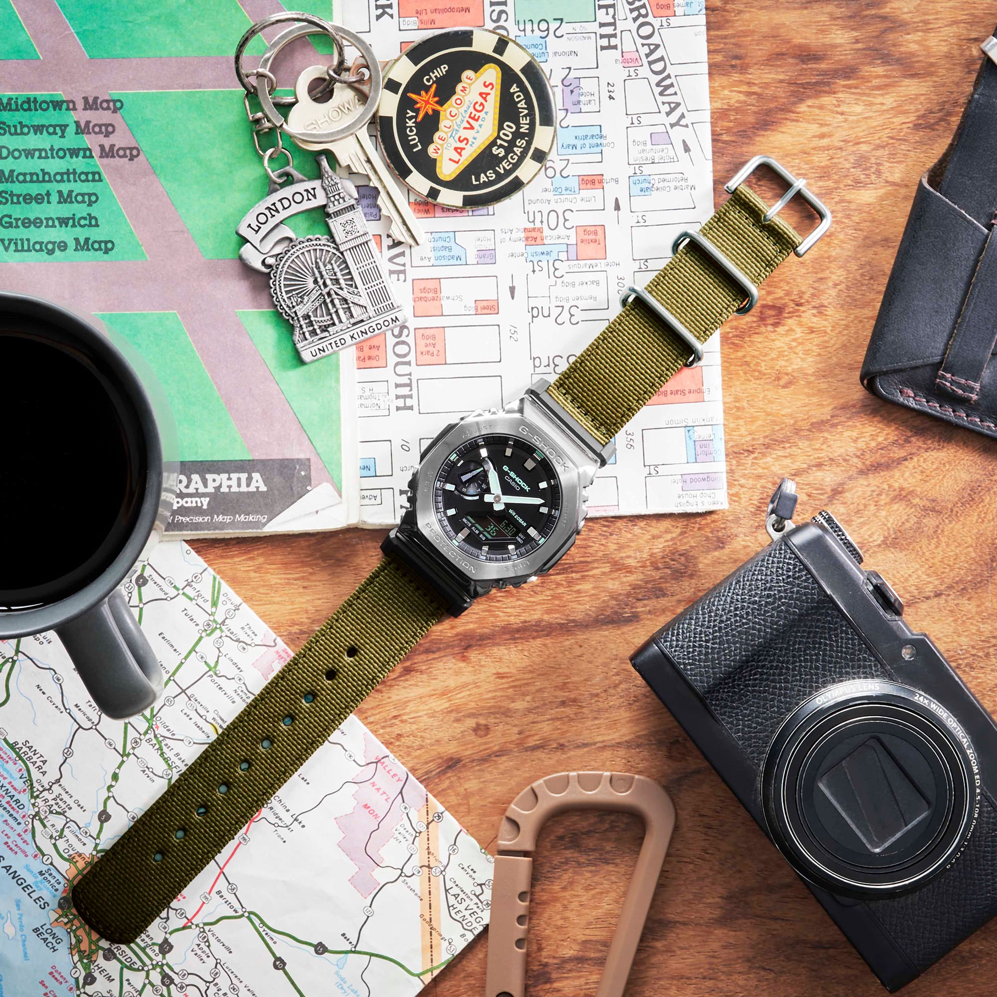 G-SHOCK GM2100CB-3A Metal covered analog digital utility watch with cloth band on a desk with map and other adventuring materials