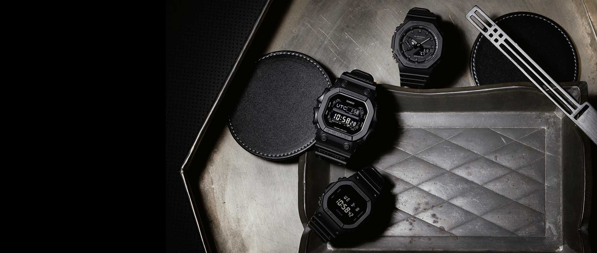 Three All Black Digital and Analog Digital G-SHOCK watches on a metal surface