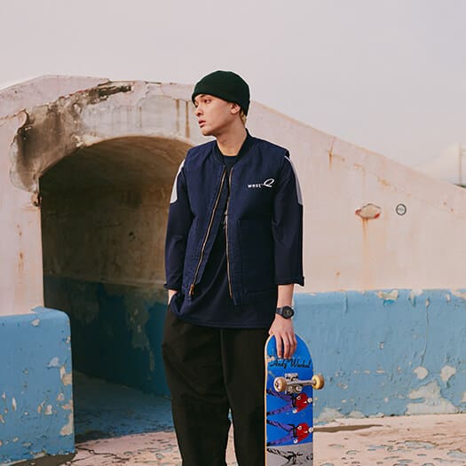 Skateboarder holding skateboard and wearing a blue G-SHOCK GAB2100 analog-digital watch in a skate park