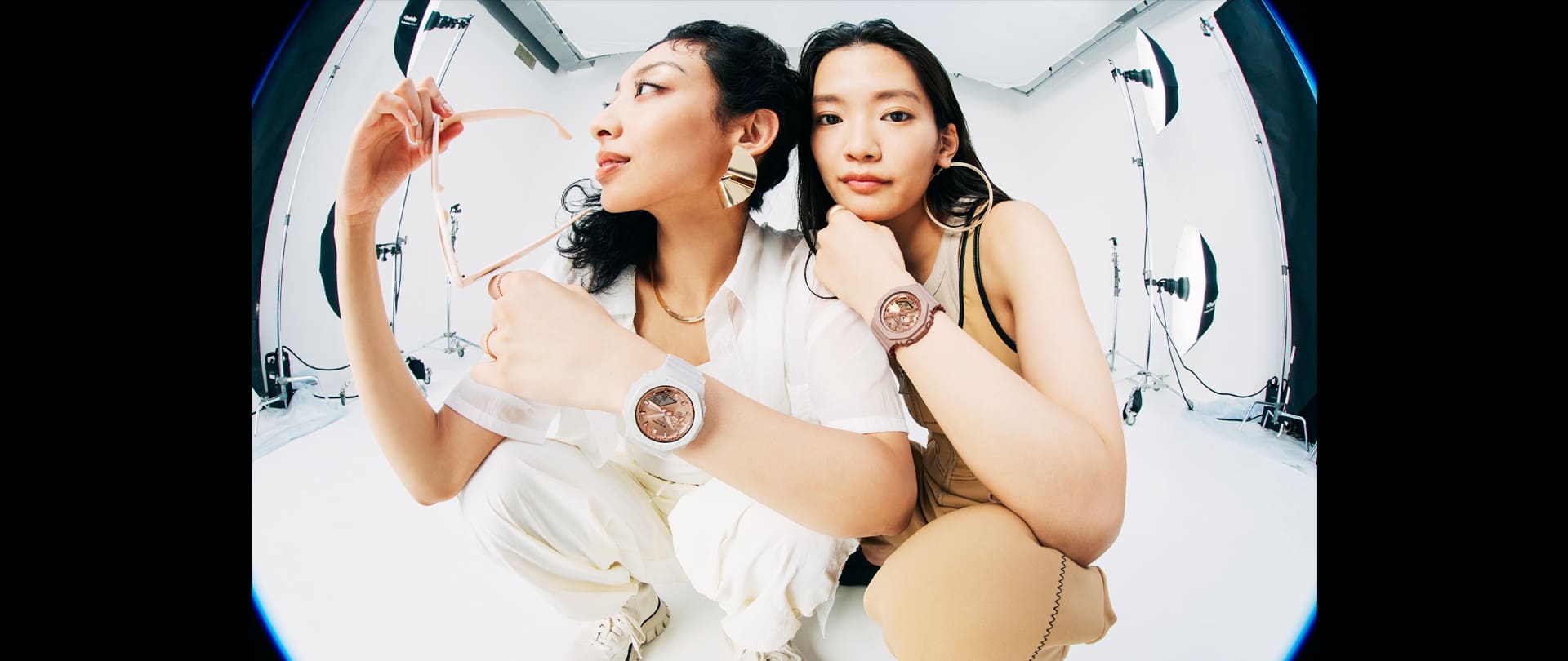 Two models wearing the G-SHOCK GMAS2100MD-7A white and GMAS2100MD-4A pink analog digital watches with pink gold face
