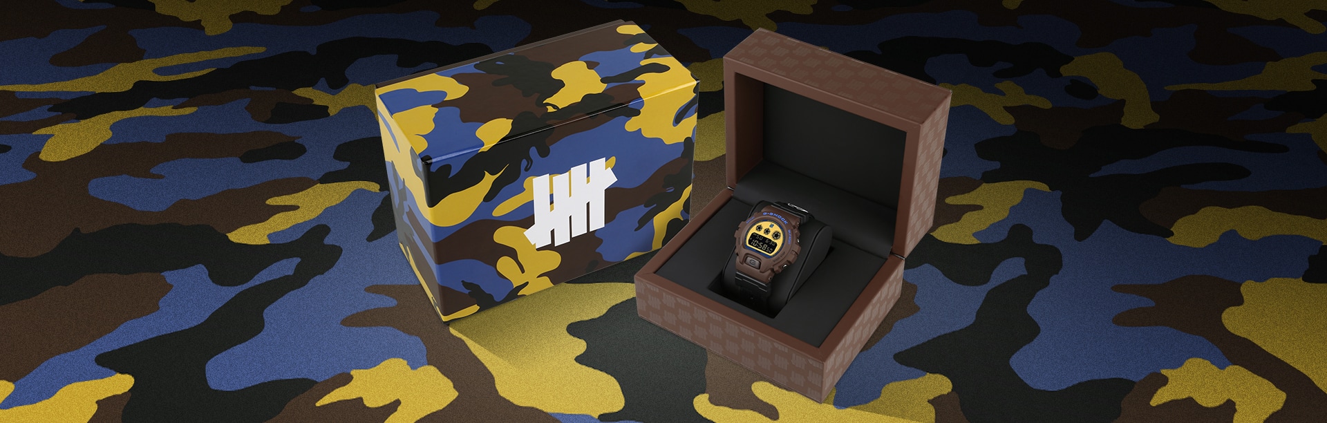 G-SHOCK x UNDEFEATED DW6900UDCR235 40th anniversary watch in its special packaging with a brown, yellow and blue camoflauge that matches the outer box design